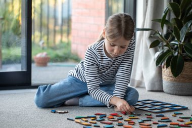 Tatlı bir kız oturma odasında yerde oturmuş mantıklı bir ahşap oyun oynuyor. Çocuk gelişimi için eko oyuncaklar