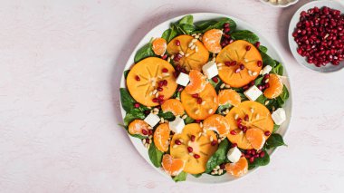 Taze hurma ve turunçgil salatası, ıspanak, feta ve pembe masada nar. Kış salatası. Noel salatası konsepti. Boşluğu kopyala