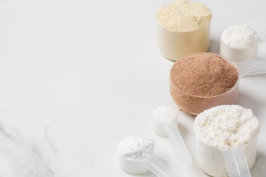 Beslenme ve zindelik için beyaz mermer zemin üzerine çeşitli protein tozu ve destek kepçeleri. Boşluğu kopyala