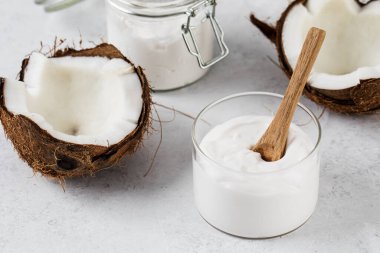 Yanında tahta kaşık ve hindistan cevizi olan cam kavanozda taze hindistan cevizli yoğurt. Vejetaryen yoğurt kavramı, laktozsuz..