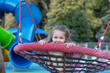 A happy girl swings on a swing at a bright playground. Playground and childhood concept.