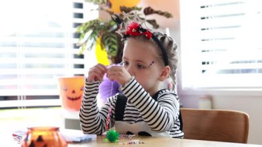 A cute girl creating halloween bead craft with Halloween costume. DIY ideas for Halloween.