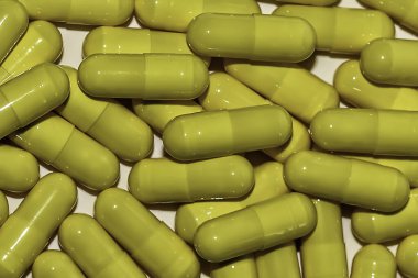 Beyaz arka planda biriken sarı hapların detaylı görüntüsü.