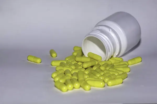 stock image Yellow capsules spilled from a medicine bottle, representing health, medication and treatment themes. Ideal for illustrating healthcare articles with space for copy.