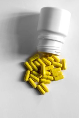 Sarı kapsüller beyaz bir şişeden beyaz bir arka plana döküldü. İlaç veya tıbbi bağlamlar için basit ve temiz bir görüntü ideal..
