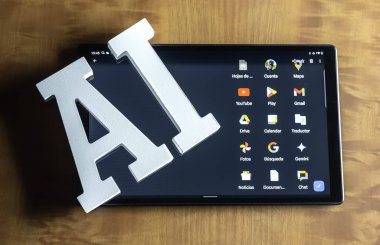 Beyaz yapay zeka harfleri ekranda Google simgelerini gösteren bir tabletin üzerinde duruyor. Dijital bir cihazda yapay zeka ve Google hizmetleri arasındaki ilişki.