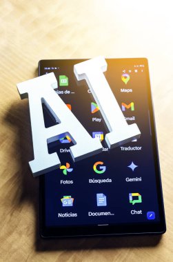 Ekranda Google simgelerini gösteren bir tablet üzerinde dinlenen beyaz yapay zeka harflerinin yakın çekimi. Dijital bir cihazda yapay zeka ve Google hizmetleri arasındaki ilişki.