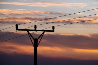 Arkaplanda günbatımı gökyüzü olan elektrik hattı çubuğu silueti detayı