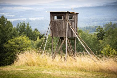 Ön planda tarlası ve arka planda tepeleri olan ahşap av kulesi