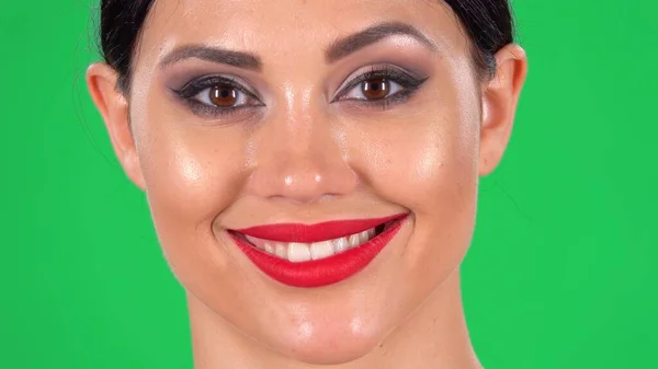 カメラを見て 笑顔と歯を明らかに美しい女性の肖像画 スタジオで緑の画面上の明るい目のメイクと赤い唇を持つブルネットの顔のクローズアップ — ストック写真