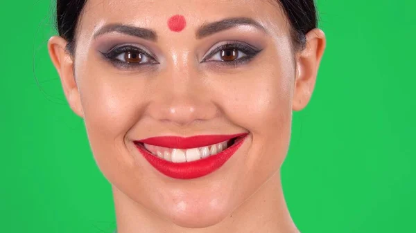 美丽的印度女人的画像 额头上有红点 看着相机 笑着露出牙齿 在工作室的绿色荧幕上用明亮的眼妆和红唇把黑发的脸合拢起来 — 图库照片