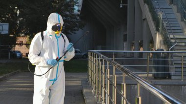 Beyaz koruyucu giysili, solunum cihazlı, kimyasalları yüzey parmaklıklarına püskürten bir sağlık çalışanı. Alkol dezenfektanı ve fıskiyeyle antiseptik ile nesneleri tedavi etmek. Hijyenik