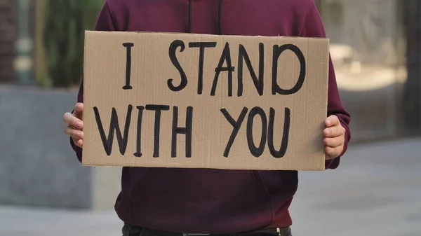 I STAND WITH YOU on cardboard poster in hands of male protester activist. Stop Racism concept, No Racism. Rallies against racism and police brutality. Peaceful life of blacks matters. City street