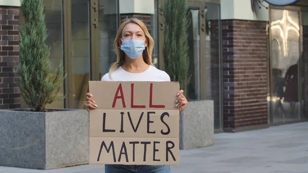 医療用マスクの若い女性は 公共の場所の屋外で段ボールのポスターですべての生活物質を立っています 抗議行動の政治活動家だ 人種差別ではなく寛容さと政治的正しさ — ストック写真