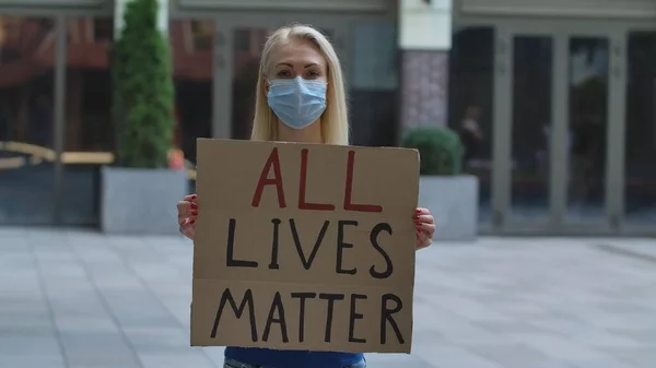 의료용 마스크를 여성은 야외의 장소에서 포스터를 시위중인 운동가 차별이 아니라 — 스톡 사진