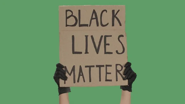 Hands of an unknown person in black gloves raise cardboard poster BLACK LIVES MATTER. Stop Racism concept, No Racism. Rallies against racism and police brutality. Peaceful life of blacks matters