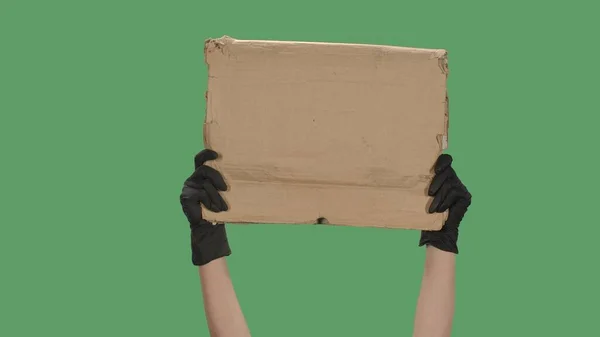 Hands in black gloves raise a blank poster made of a cardboard box. Empty space for your text, logo or advertisement. Banner design concept. Isolated a green screen, chroma key