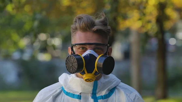 穿着白色防护服 眼镜和呼吸器的男人的画像 在城市街道的背景上看着相机 病毒学家或医务工作者在公园的室外活动 Covid 19疾病爆发概念 — 图库照片