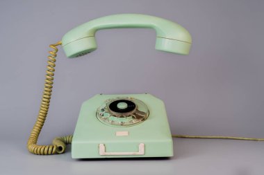 Gri arka planda asılı ahizesi olan eski mavi, döner telefon. Çevirmeli, kablolu ve alıcı cep telefonlu klasik ev telefonu. İletişim, haberleşme.
