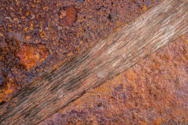 Ahşap bir tahtanın üzerinde iki tabak çürümüş metal var. Demir pas ve eski ahşap dokular. Sarı ve turuncu aşınma desenli paslı kahverengi metal bir levhanın makro görüntüsü.