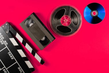 CD, film şeridi, siyah plastik VHS video kaset ve pembe arka planda alkışlama tahtası. Eski depolama medyası, video ya da film izleme ya da müzik dinleme dürtüleri. Örneksel film ve