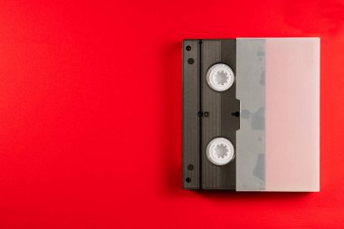 Kırmızı arka planda beyaz bir çantada siyah VHS video kaset. Analog manyetik bantlı plastik retro video kaset. Fotoğrafınız için çalışma alanı olan eski bir film kasetinin üst görünümü
