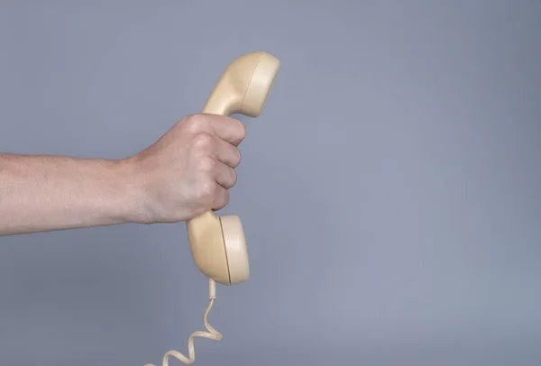 灰色の背景に古い黄色のプラスチック製の電話受信機を保持男性の手 男の手にレトロなロータリーホーム電話からリモート携帯電話を閉じます コミュニケーション 会話の概念 — ストック写真