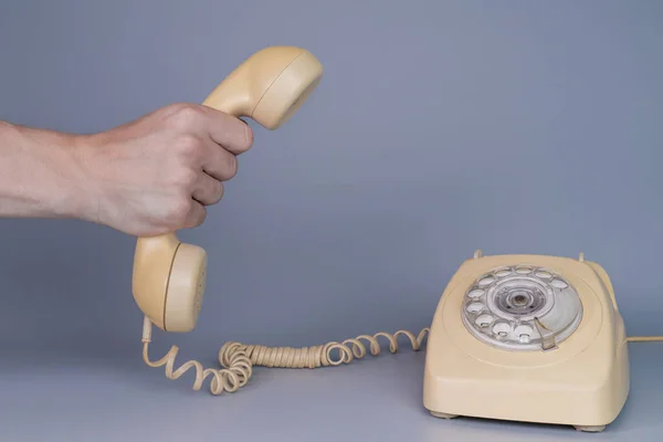灰色の背景にロータリー電話の近くに古い黄色のプラスチック製の電話受信機を保持男性の手 男の手の中にレトロな家庭用電話装置からのリモート携帯電話を閉じます — ストック写真