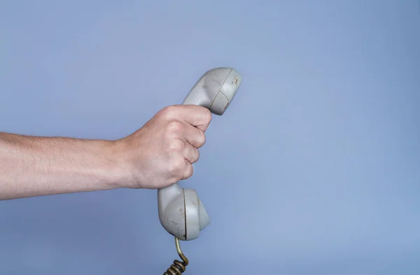 青い背景に古いグレーのプラスチック製の電話受信機を保持男性の手 男の手にレトロなロータリーホーム電話からリモート携帯電話を閉じます コミュニケーション 会話の概念 — ストック写真