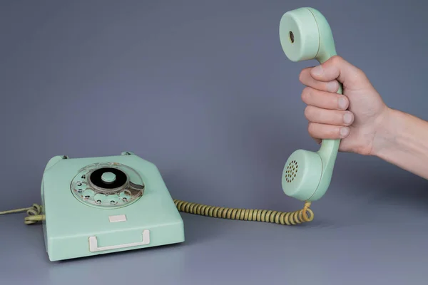 男性の手は灰色の背景にロータリー電話の近くに古い青のプラスチック製の電話受信機を保持 男の手の中にレトロな家庭用電話装置からのリモート携帯電話を閉じます コミュニケーションの概念 — ストック写真