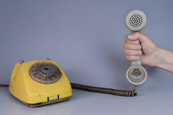 Mężczyzna Trzyma Starą Plastikową Słuchawkę Pobliżu Żółtego Telefonu Obrotowego Szarym — Zdjęcie stockowe