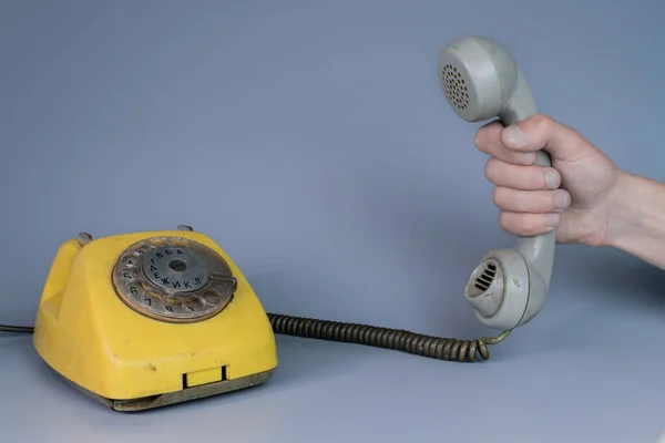 Mężczyzna Trzyma Starą Plastikową Słuchawkę Pobliżu Żółtego Telefonu Obrotowego Szarym — Zdjęcie stockowe