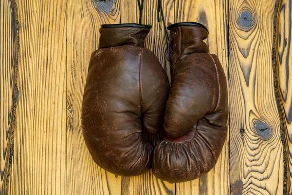 Old brown leather boxing gloves hanging on wooden vintage background. A pair of shabby, aged boxing gloves is retire. Close up of worn sports mittens for wrestling on wooden background without anyone