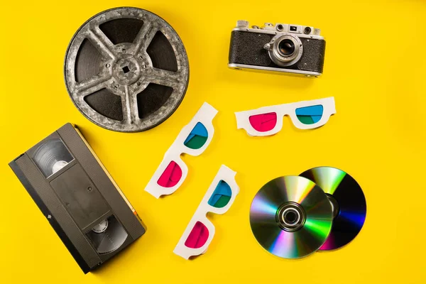 新彩虹光盘 电影带Bobbin和复古相机 黄色背景的黑色塑料Vhs盒式磁带和硬纸板3D眼镜 旧的存储介质 模拟电影和数字复古 — 图库照片