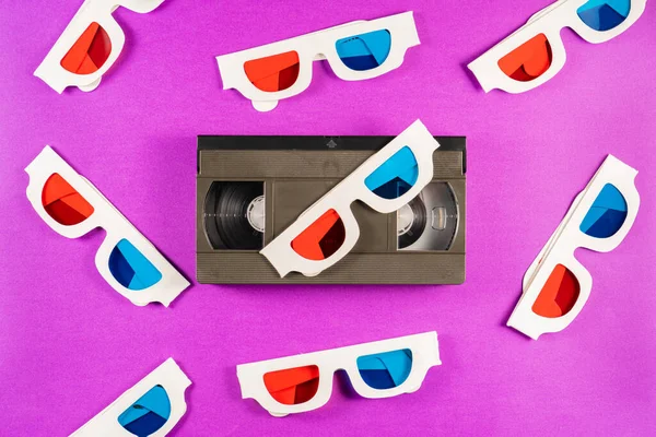 旧的白纸3D眼镜 蓝色的红色镜片和紫色背景的黑色录像带 带磁带和立体三维硬纸板眼镜的复古盒式磁带 古董店的背景 — 图库照片