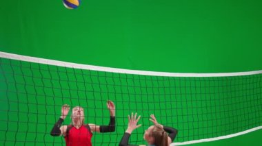 Spor giyimli iki genç kadın yeşil ekran krom anahtarıyla voleybol oynuyor. Bir atlet kalenin üzerinden topa vuruyor ve rakibi topu kaçırıyor. Saldırı ve savunma becerileri pratiği. Spor yaşam tarzı.