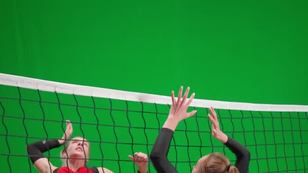 緑色の画面のクロマキーでバレーボールをしているスポーツウェアの2人の若い女性 1人の選手がボールに当たり もう1人はネット上でそれを打つ 攻撃力と防御力の練習 スポーツライフスタイル スポーツ — ストック動画