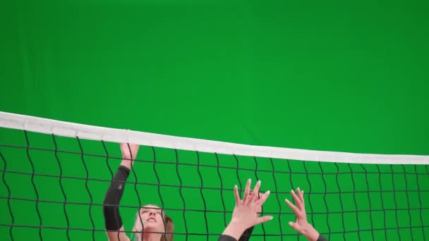 緑色の画面のクロマキーでバレーボールをしているスポーツウェアの2人の若い女性 1人の選手がネット上でボールを打ち負かし 相手はボールを逃す 攻撃力と防御力の練習 スポーツライフスタイル — ストック動画