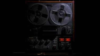 Siyah stüdyo arka planında klasik makaradan makaraya kayıt cihazı. Karanlıkta bir ışık demeti tarafından aydınlatılmış eski plastik kutuları olan Retro müzik çalar. Ön manzara. Popüler disko eğilimleri 70 'ler, 80' ler