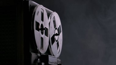 Siyah stüdyo arka planında dumanlı bir teyp kaydı. Müzik çalmak için manyetik teybi olan analog antika müzik çalar. Karanlıktaki eski çember bobbin. Retro grubu, eski haline dön.