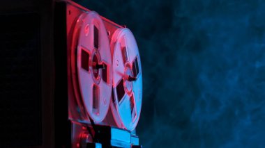 Stüdyonun arka planında, mavi pembe ışık ve dumanlı bir teyp var. Müzik çalmak için manyetik teybi olan analog antika müzik çalar. Karanlıktaki eski çember bobbin. Retro partisi