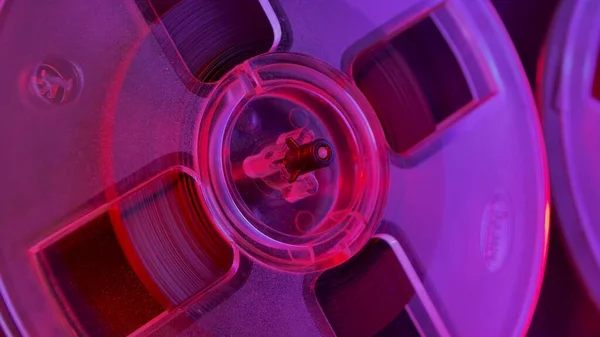老式模拟卷筒到卷筒录音机上的透明塑料卷筒 旧圆筒 带着复古带子 闪烁着紫罗兰色的粉红灯光 复古派对靠近点 — 图库照片