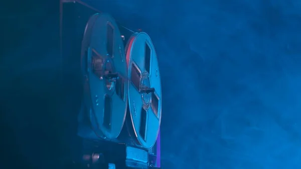 在带蓝光和烟雾的工作室背景上旋转卷轴录音机 具有磁带卷轴的模拟古董唱机 用于播放音乐 黑暗中的旧圆筒 复兴党 — 图库照片