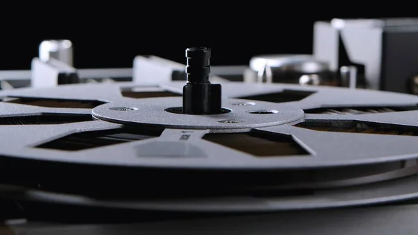 Reel to reel tape recorder on black background. Macro shot of vintage music player with round metallic bobbins. Retro magnetic tape reel. Popular disco trends 70s, 80s. Side view