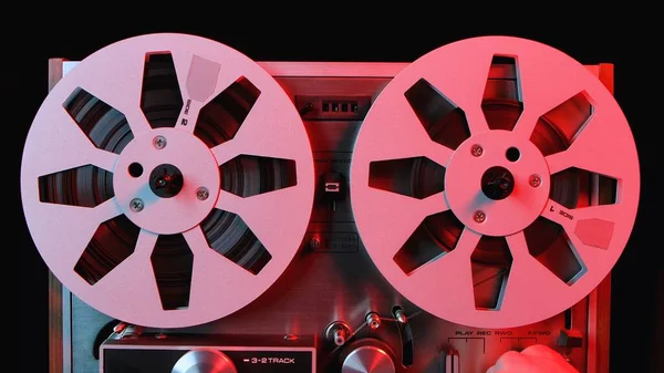 用红光照明的卷筒到卷筒录音机 接近老式音乐播放器与两个圆形金属箱 复古磁带卷轴 流行的迪斯科趋势70 80年代 — 图库照片
