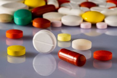 Farklı renkte haplar ve tabletler parlak yansıtıcı bir yüzeye saçılmış. Beyaz, sarı, kahverengi ve yeşil ilaçları kapatın. Antibiyotikler, vitaminler, ağrı kesiciler. Tıbbi geçmişin
