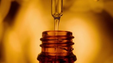 Bir damla sıvı, yağ, ilaç ya da kahverengi şişedeki tıbbi cam pipetten damlayan bir sıvı. Serum damlıyor ve bulanık sarı arka planda bir pipetin içinde hava kabarcıkları oluşturuyor. Tıp kavramı