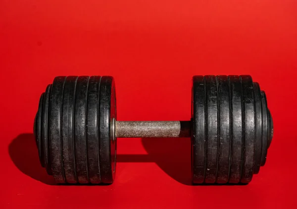 重量训练设备 沉重的黑色哑铃躺在红色的背景上 投下了阴影 交叉配合 力量训练的运动杠铃 在健身房锻炼 — 图库照片