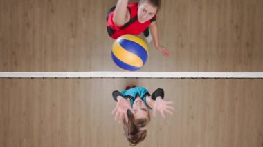 Çocuk parkında voleybol oynayan iki genç bayan sporcu. Top servis yapan bir kadın ve topa vuran ve zaferle sevinen bir rakip. Mavi ve kırmızı üniformalı kadın oyuncular