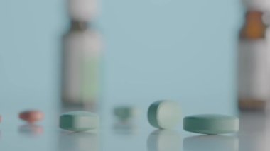 Yuvarlak kahverengi haplar mavi arka plandaki masaya saçılmış. Tabletler ve çeşitli tıbbi şişelerle birlikte masanın üzerinde kamera hareketi. Vitaminler, antibiyotikler ve ağrı kesicileri kapatın. Yavaş çekim
